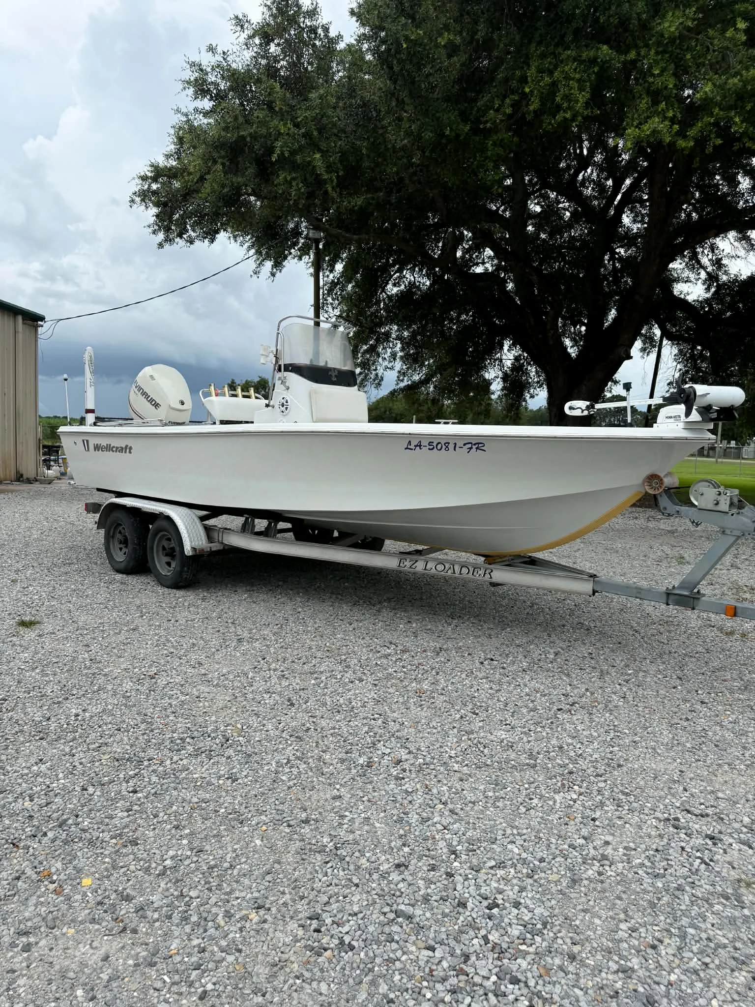 Detailed white Wellcraft boat on a trailer beneath a large oak tree